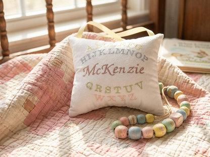 Decorative music box pillow with embroidered name on a quilted surface