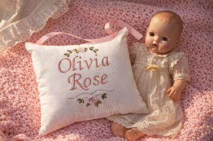 Vintage doll in a lace dress next to a music box pillow with 'Olivia Rose' embroidery on a pink textured background