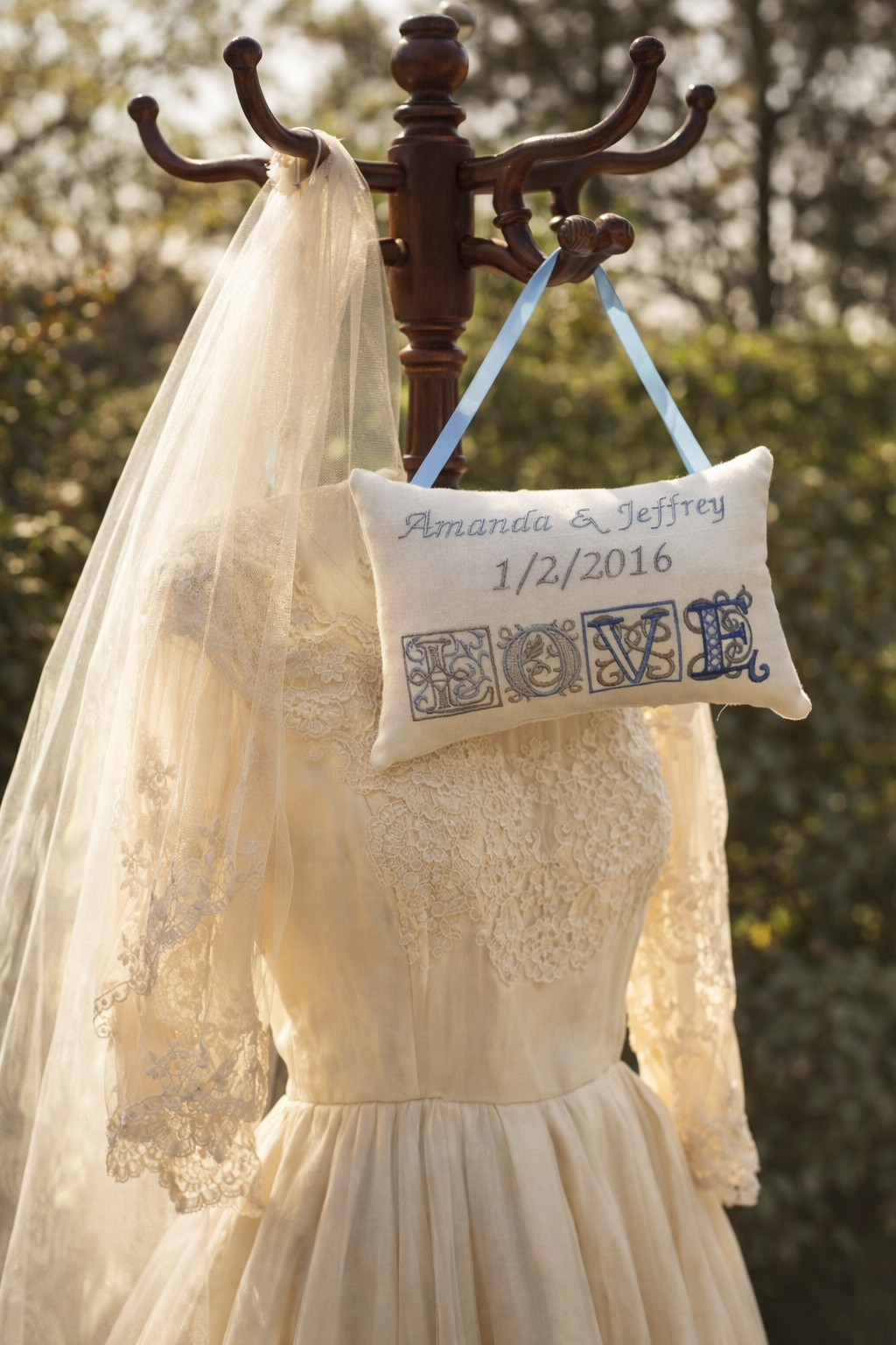 Wedding dress with veil and personalized music box pillow hanging on a coat rack outdoors.