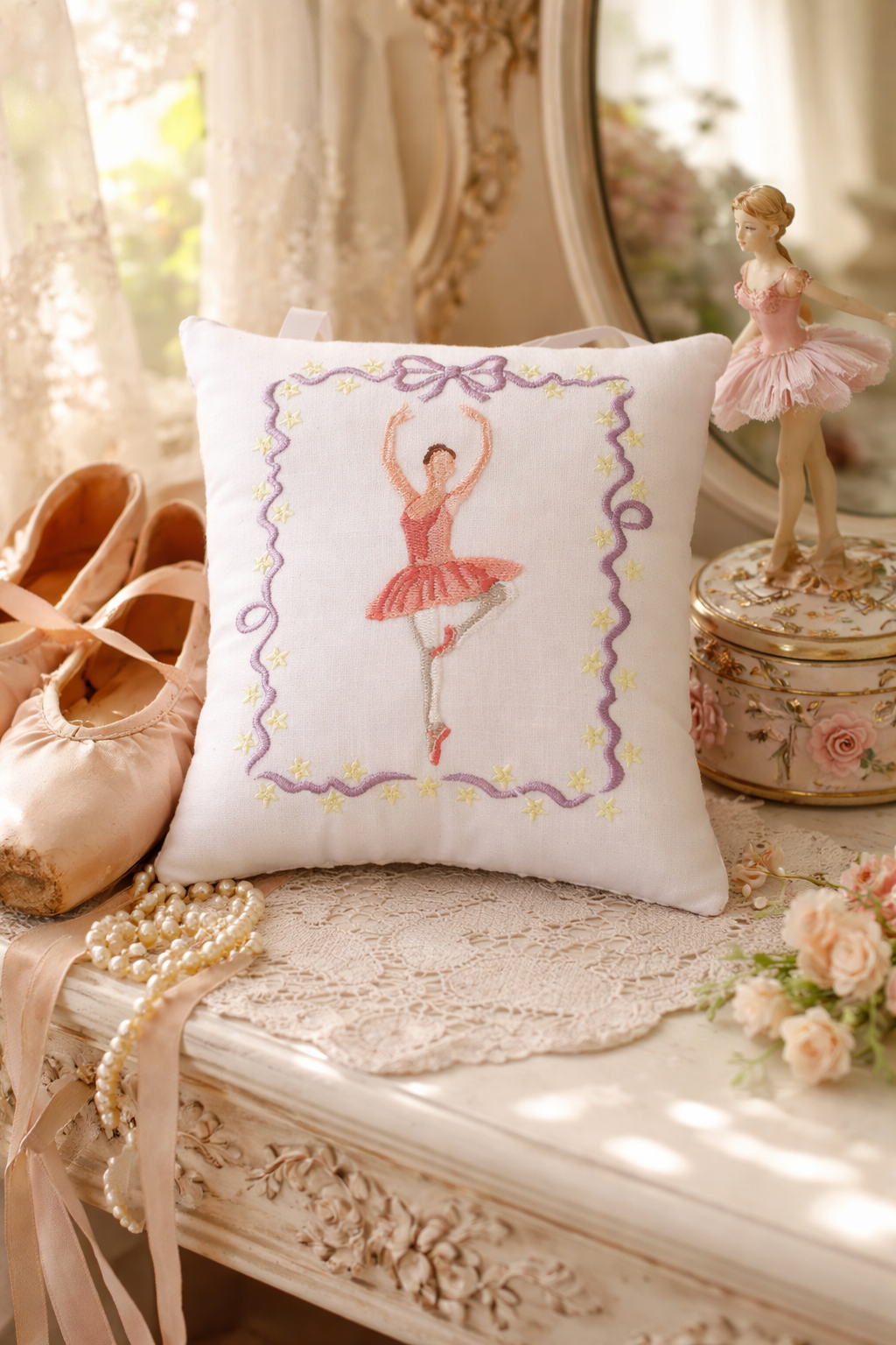 Decorative music box pillow with a ballerina design on a vanity table with ballet shoes and figurines.