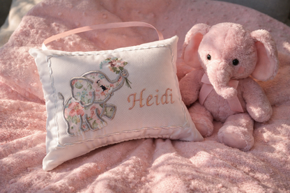 Floral elephant design music box pillow with embroidered name 'Heidi' on a pink blanket with a plush toy elephant.