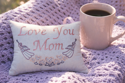 Decorative music box pillow with 'Love you Mom' text and a mug of coffee on a textured surface.