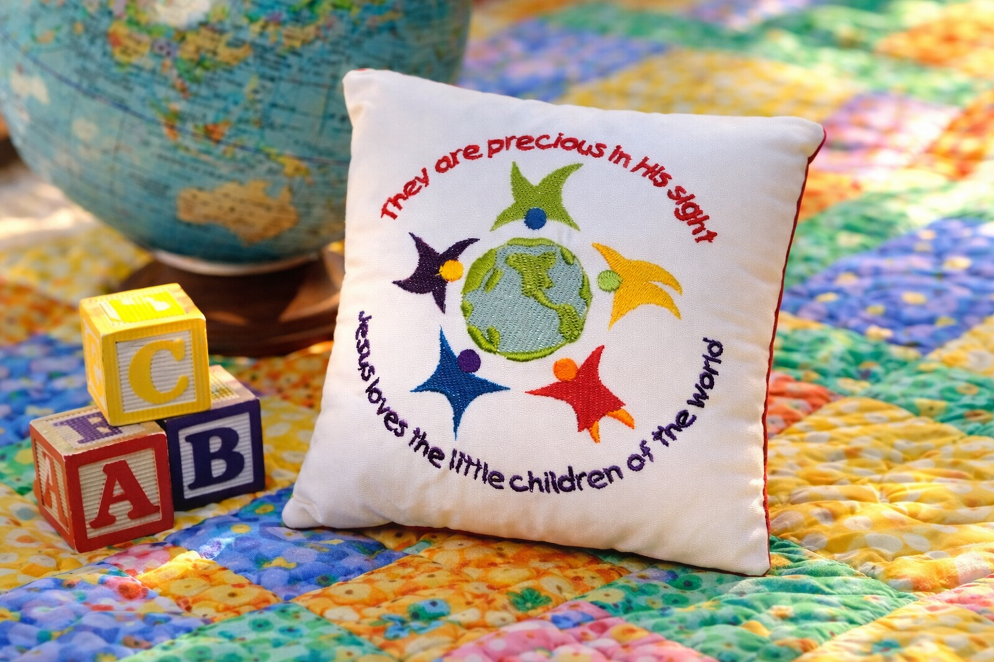 Decorative music box pillow with colorful design and text on a multicolored quilt with alphabet blocks and a globe.