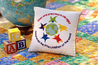 Decorative music box pillow with colorful design and text on a multicolored quilt with alphabet blocks and a globe.