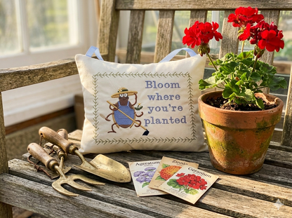 Decorative music box pillow with gardening-themed design, potted plant, and gardening tools on a wooden surface.