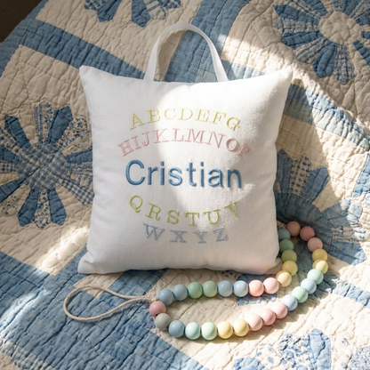 Decorative music box pillow with embroidered name on a quilted surface