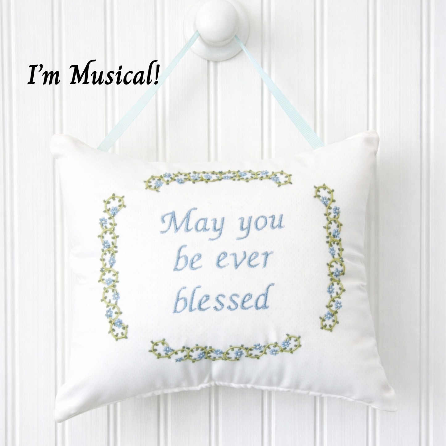 Decorative music box pillow with embroidered text and floral border on a white background