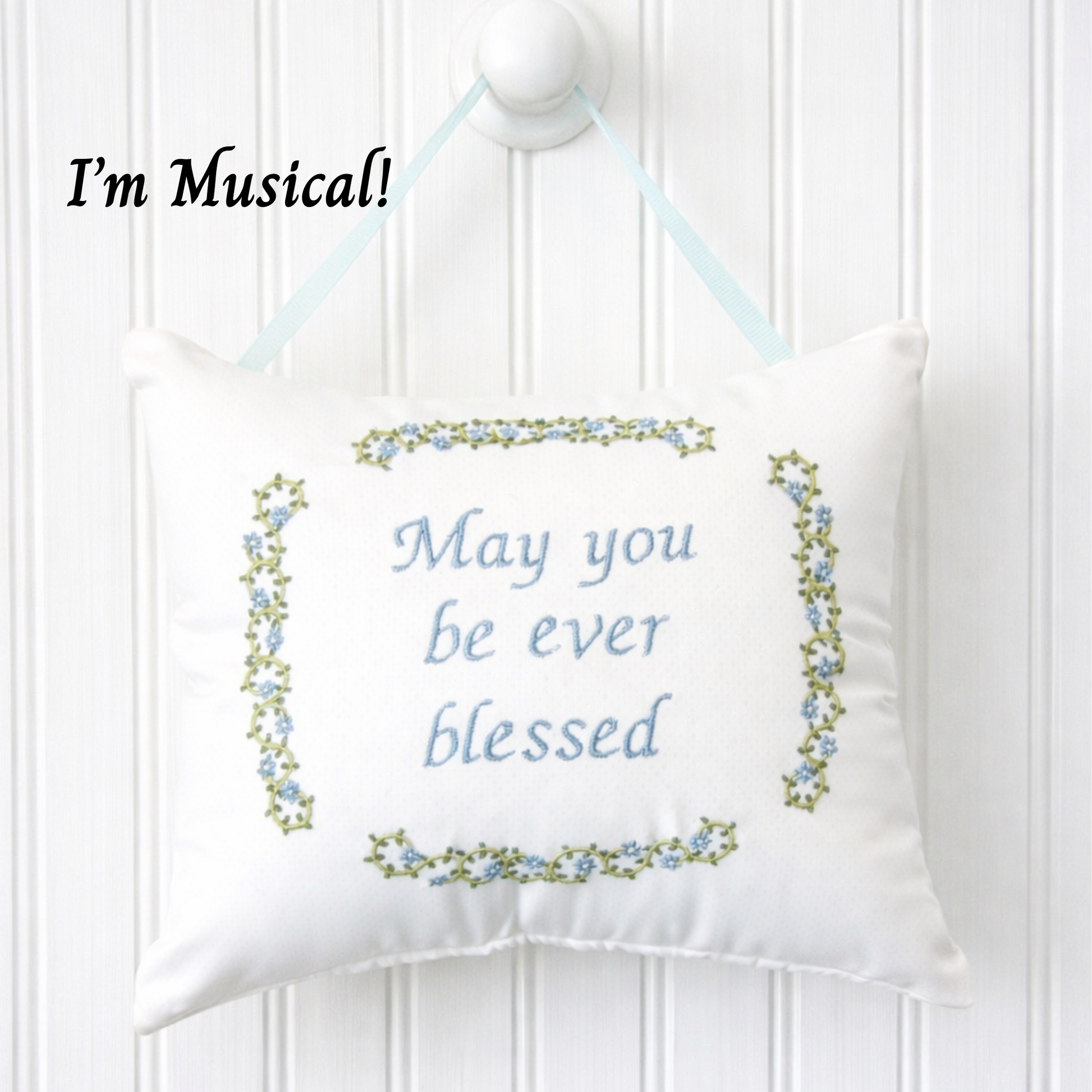 Decorative music box pillow with embroidered text and floral border on a white background