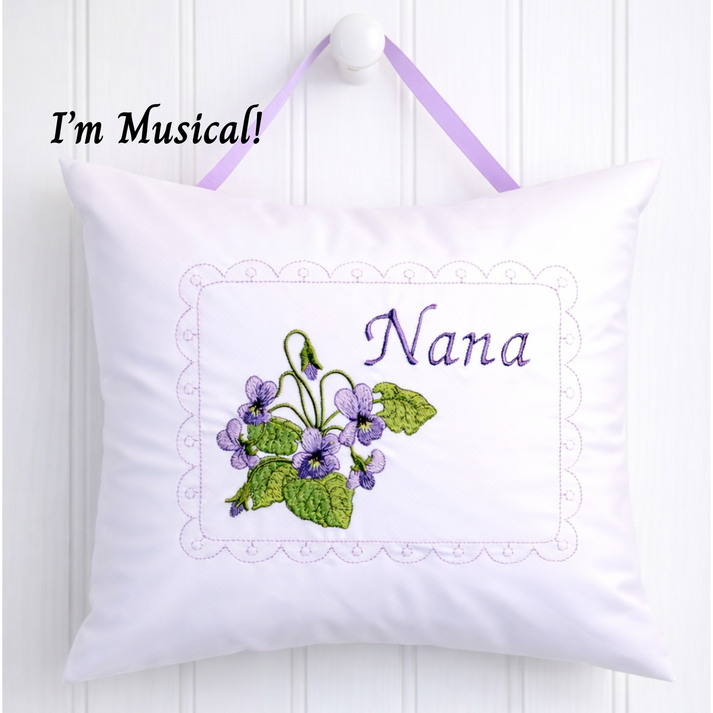 White music box pillow with floral design and 'Nana' text, hanging on a white wall.