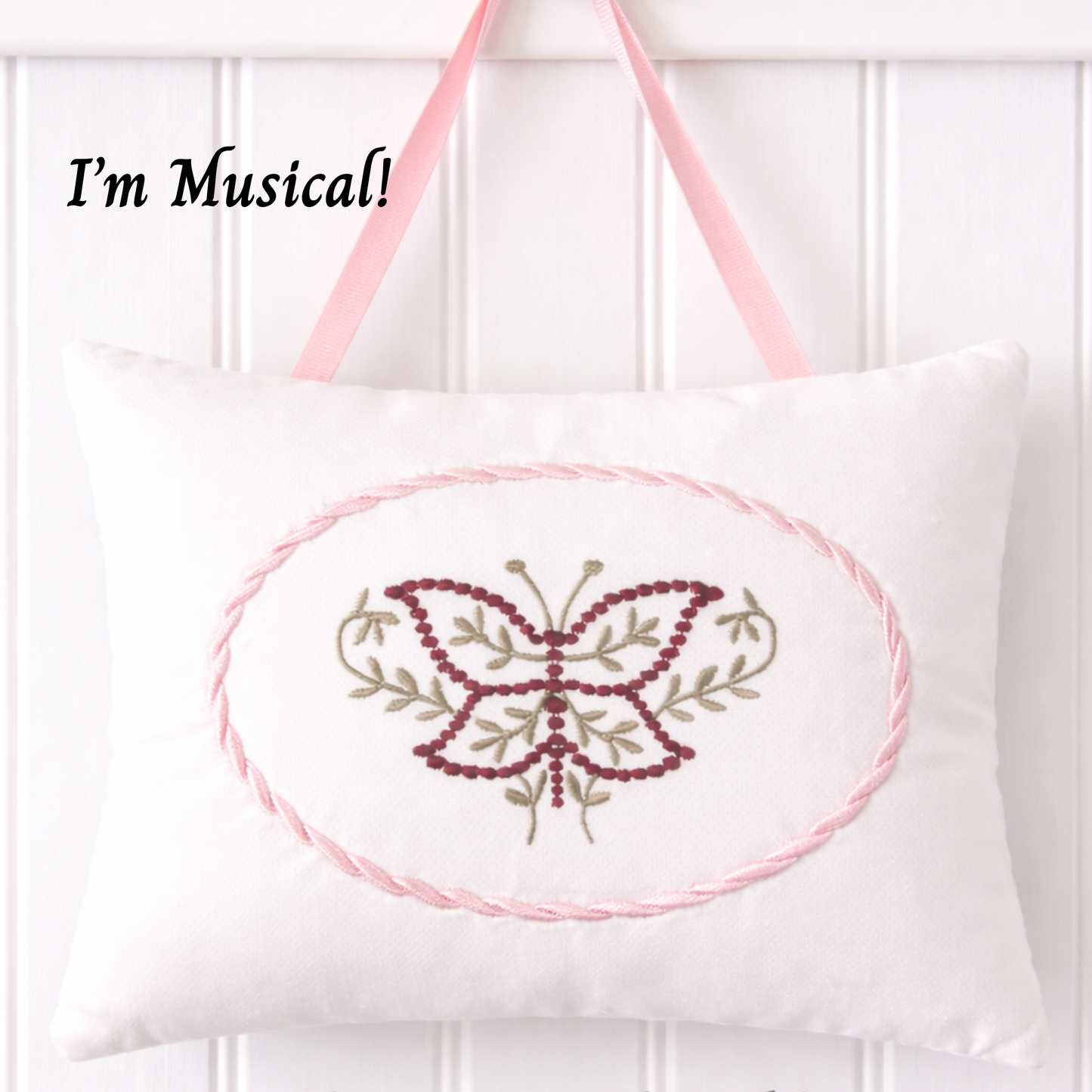 White music box pillow with embroidered butterfly design and pink straps on a white background