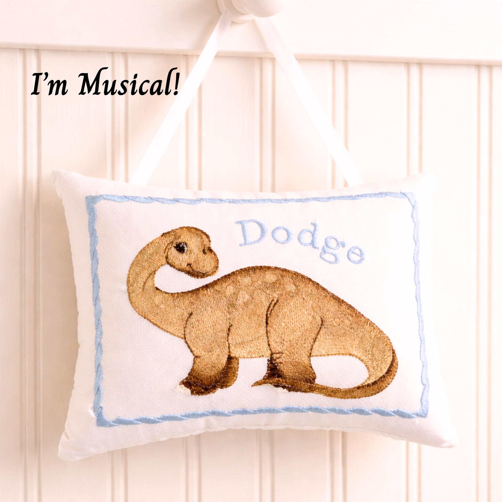 Decorative music box pillow with a dinosaur design and the name 'Dodge' on a white background.