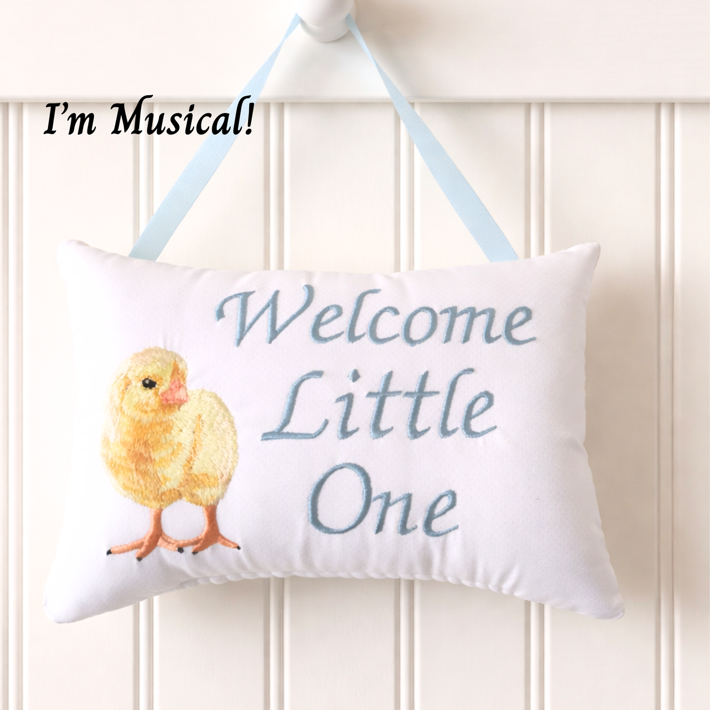 Decorative music box pillow with a chick illustration and text 'Welcome Little One' on a white background.