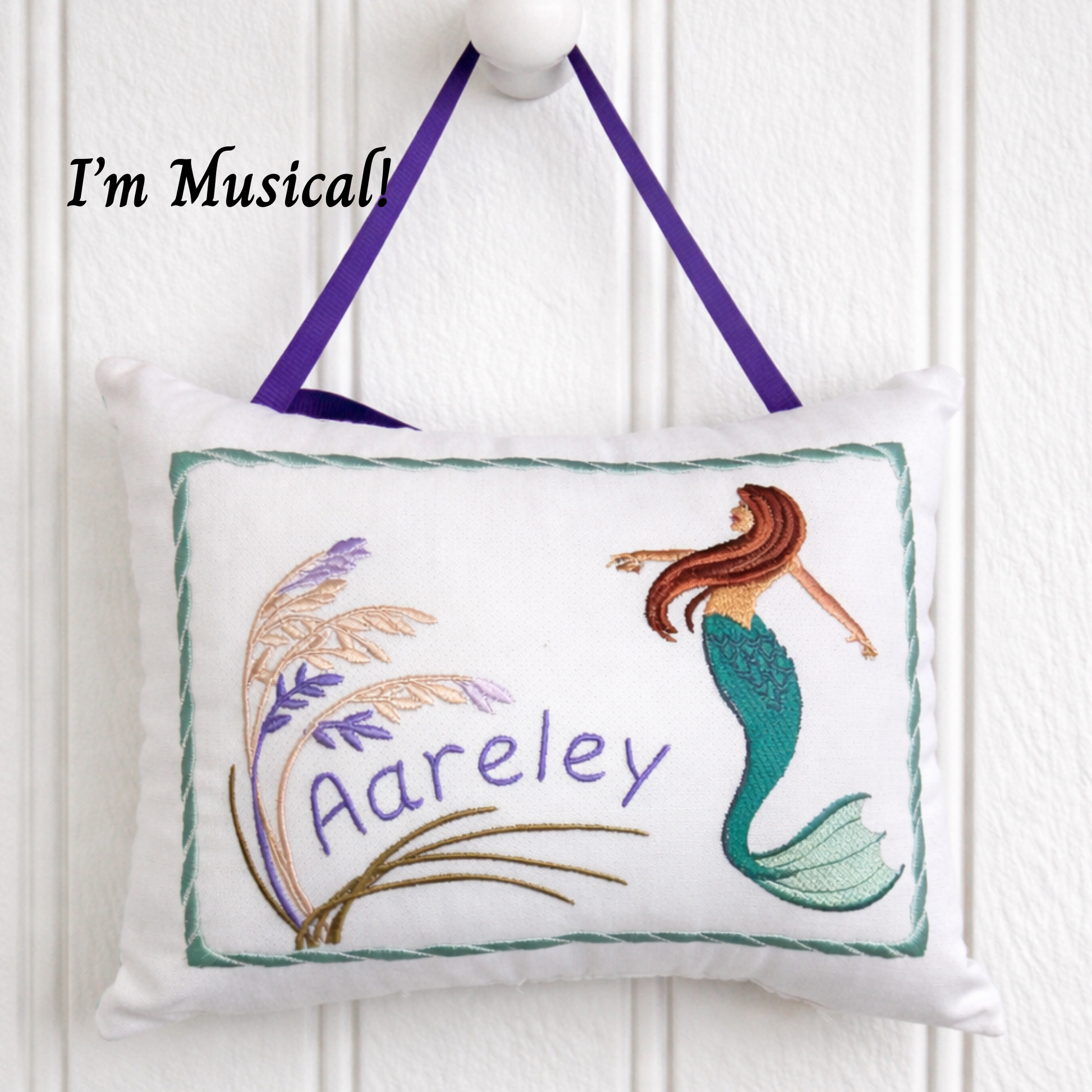 Embroidered music box pillow with mermaid design and 'Aareley' text on a white background