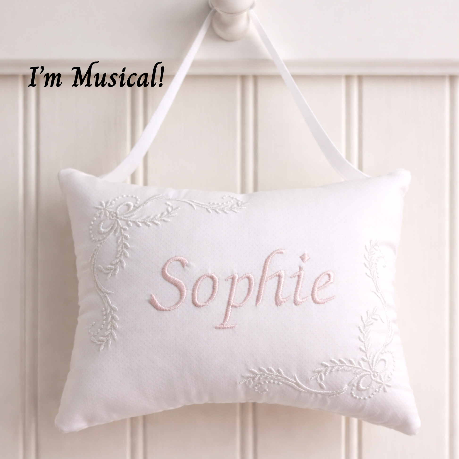 White music box pillow with embroidered name 'Sophie' on a white wooden panel background