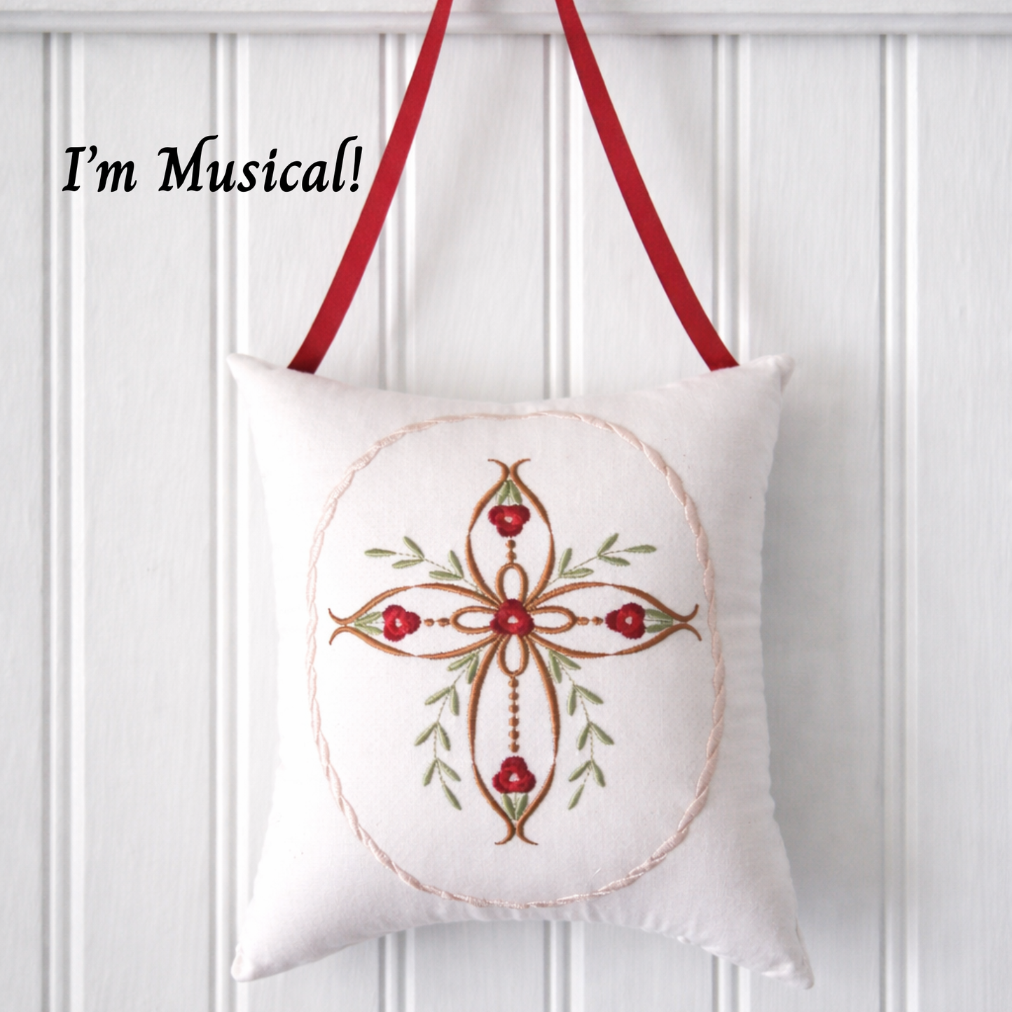 Decorative music box pillow with embroid cross and red roses on a white paneled wall.
