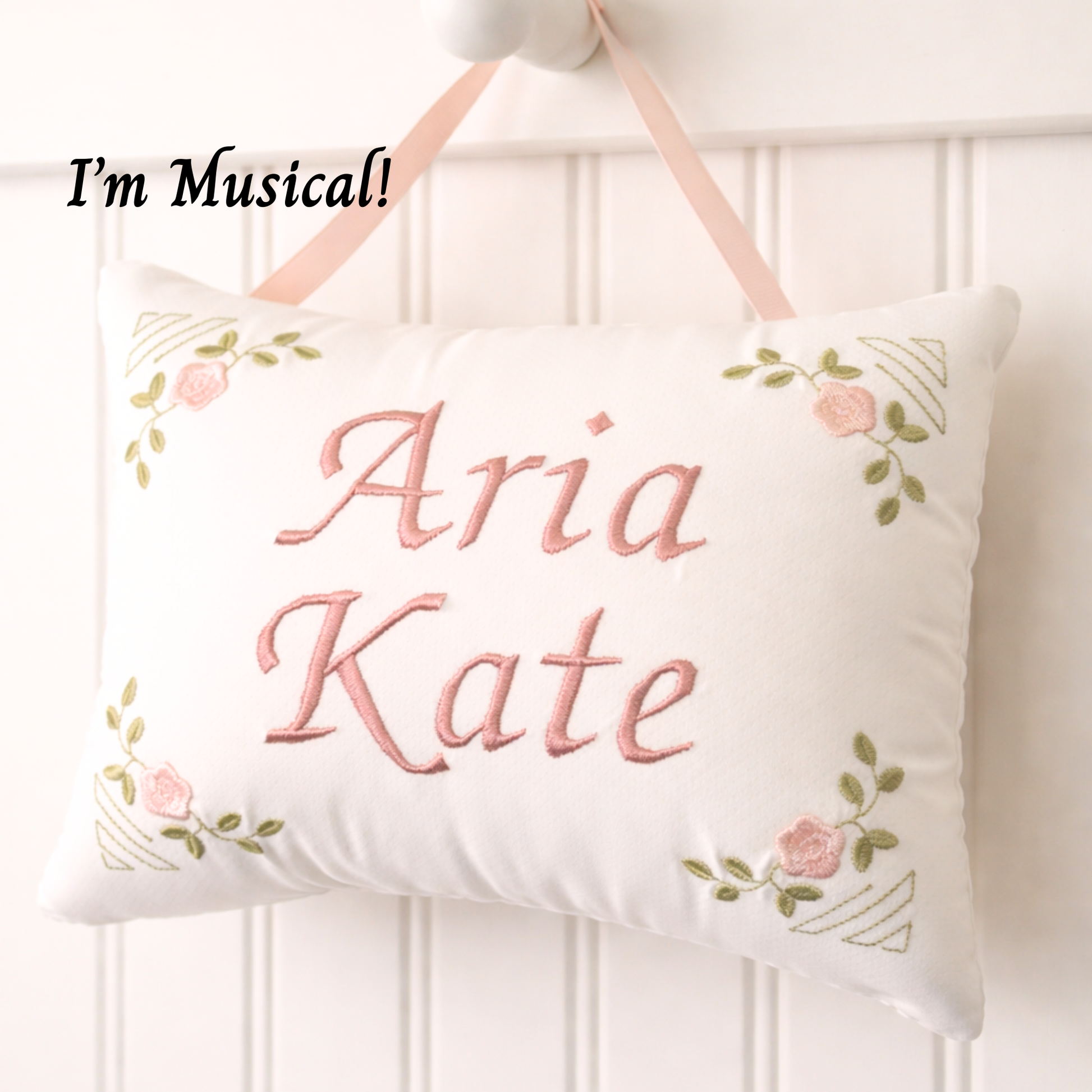 Decorative music box pillow with embroidered names 'Aria' and 'Kate' on a white background