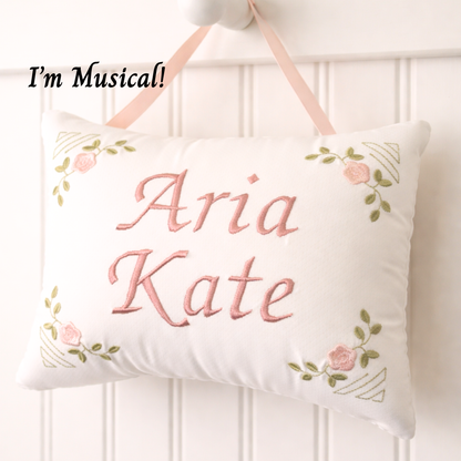 Decorative music box pillow with embroidered names 'Aria' and 'Kate' on a white background