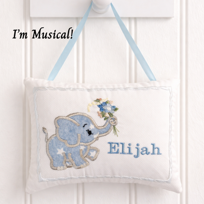 Decorative hanging music box pillow with a blue elephant and floral bouquet, personalized with 'Elijah', on a white background.
