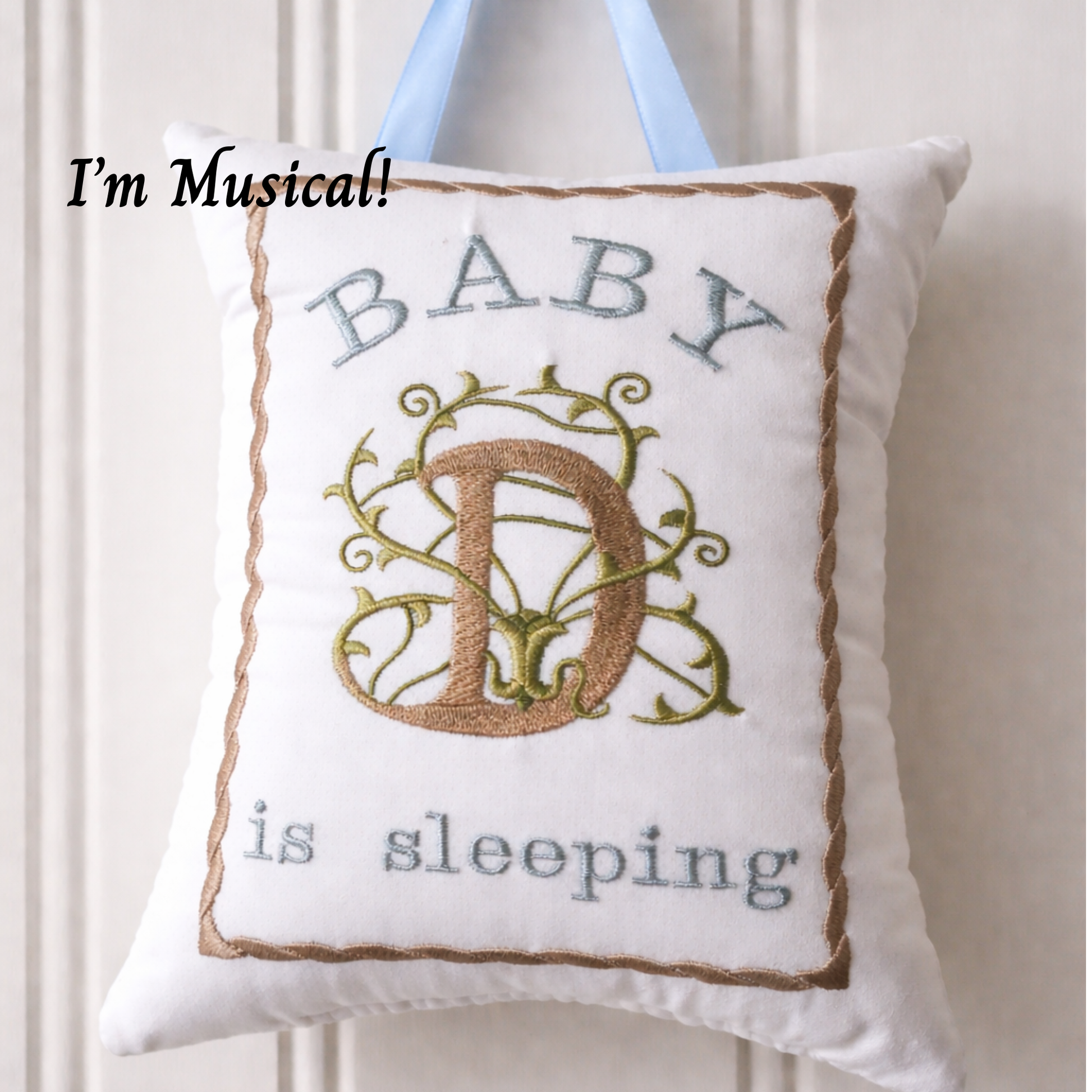 Decorative music box pillow with 'BABY D is sleeping' text and embroidered letter 'D' on a white background.