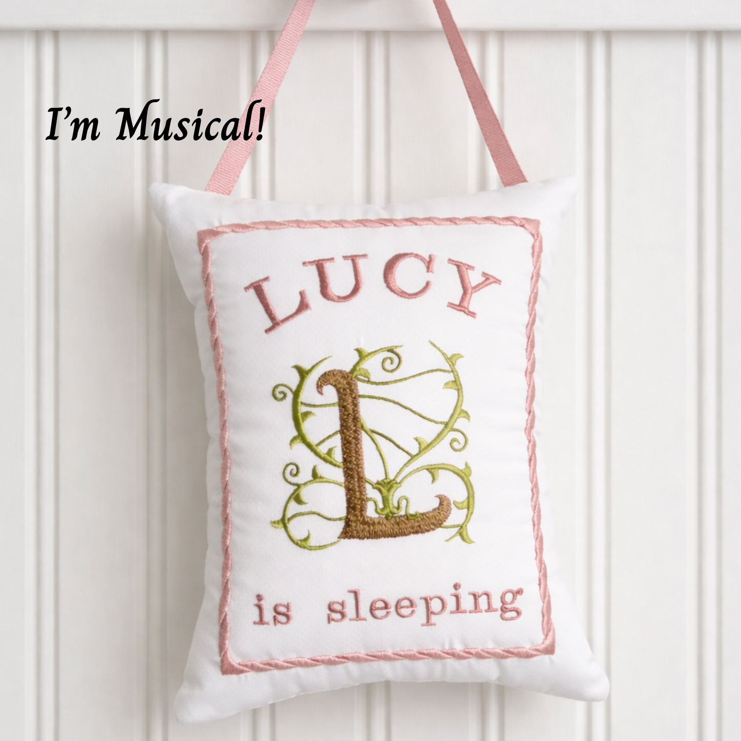 Decorative music box pillow with 'LUCY is sleeping' text and a decorative letter 'L' on a white background.