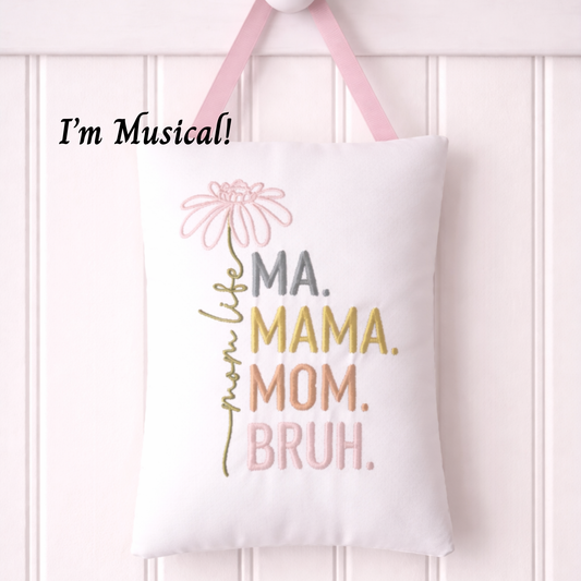 White musical pillow with colorful text and a pink flower graphic, hanging against a white background.