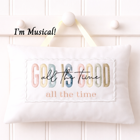 Embroidered music box pillow with colorful text 'GOD IS GOOD all the time' on a white background.