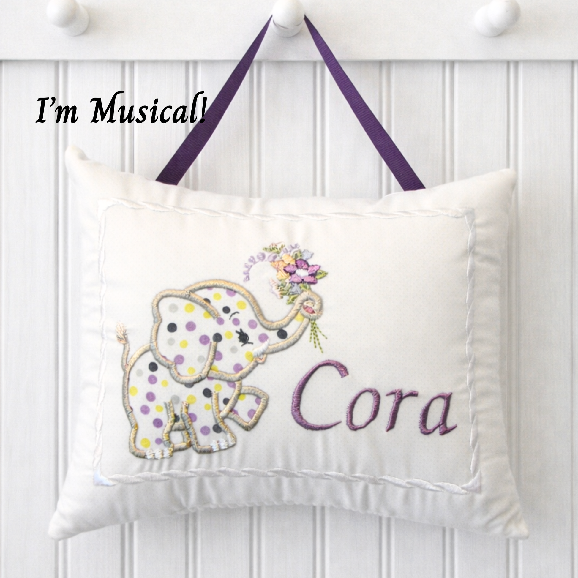 Decorative music box pillow with an elephant design and the name 'Cora' on a white background.