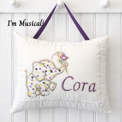 Decorative music box pillow with an elephant design and the name 'Cora' on a white background.