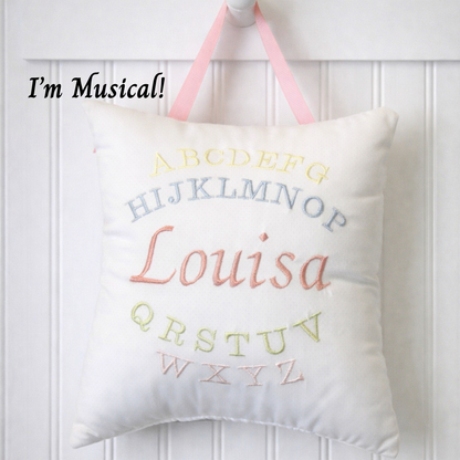 Decorative music box pillow with embroidered letters and name 'Louisa' on a white background