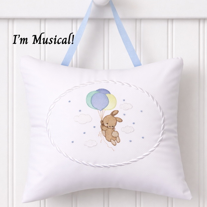 White music box pillow with embroidered bunnyr and balloons design, hanging against a white background.