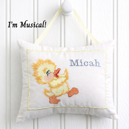 Embroidered music box pillow with a duck design and the name 'Micah' on a white background.