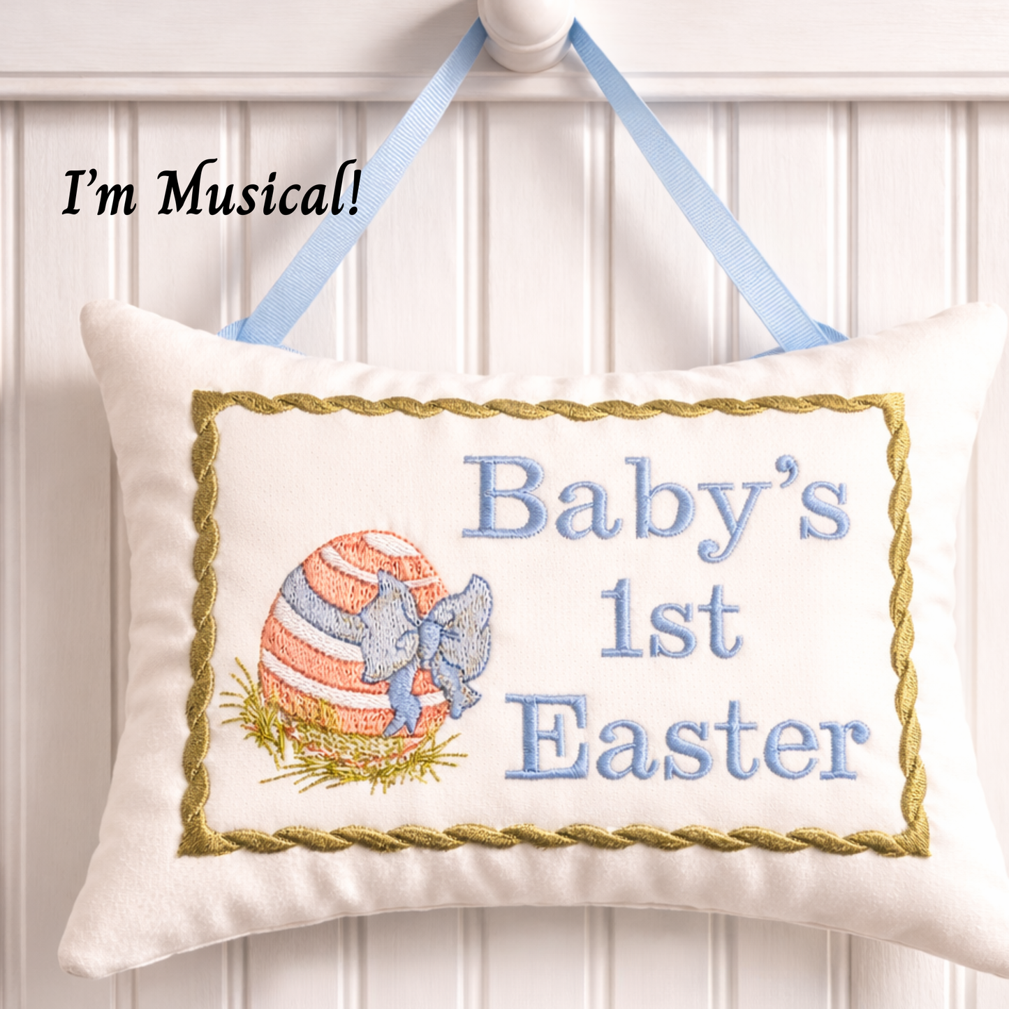 Decorative music box pillow with embroidered text and Easter design, hanging on a white wall.