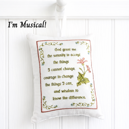 Decorative music box pillow with embroidered text and design on a white background