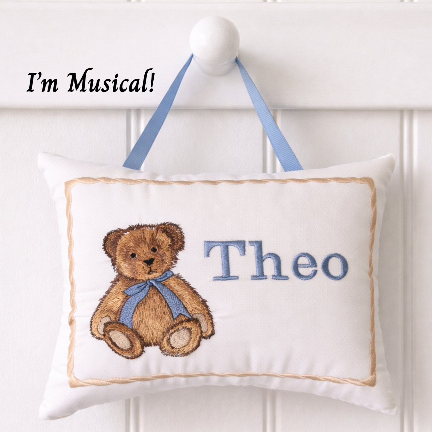 Decorative music box pillow with teddy bear design and name 'Theo' on a white background