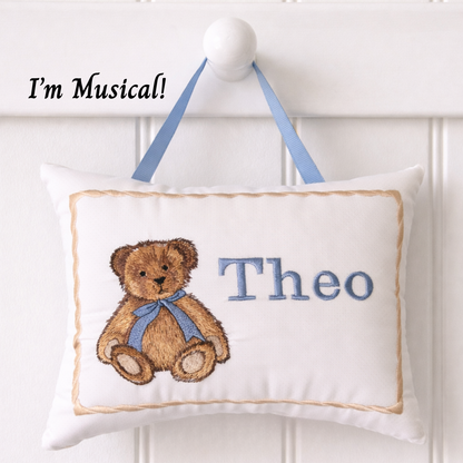 Decorative music box pillow with teddy bear design and name 'Theo' on a white background