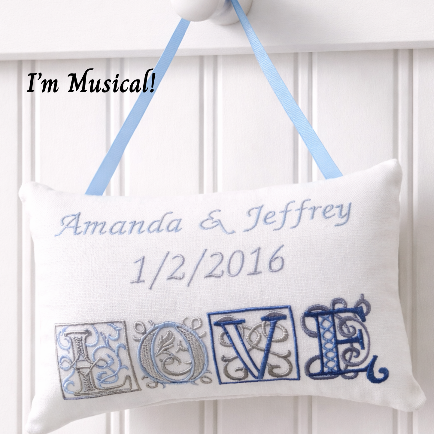 Decorative music box pillow with embroidered 'LOVE' and personalized text, hanging against a white background.