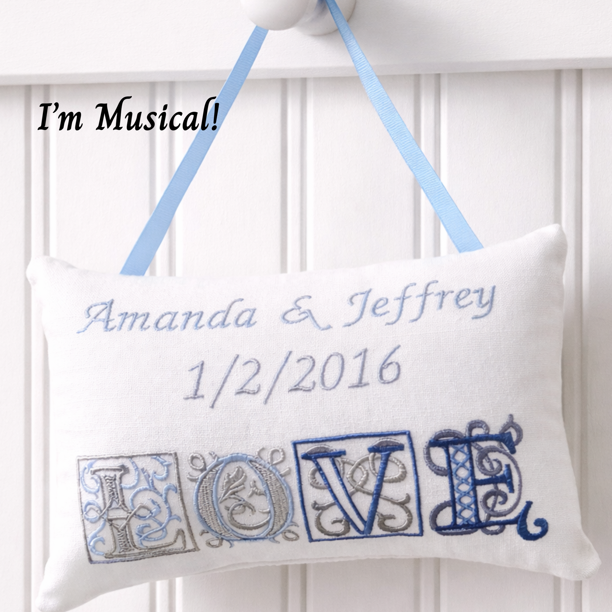 Decorative music box pillow with embroidered 'LOVE' and personalized text, hanging against a white background.