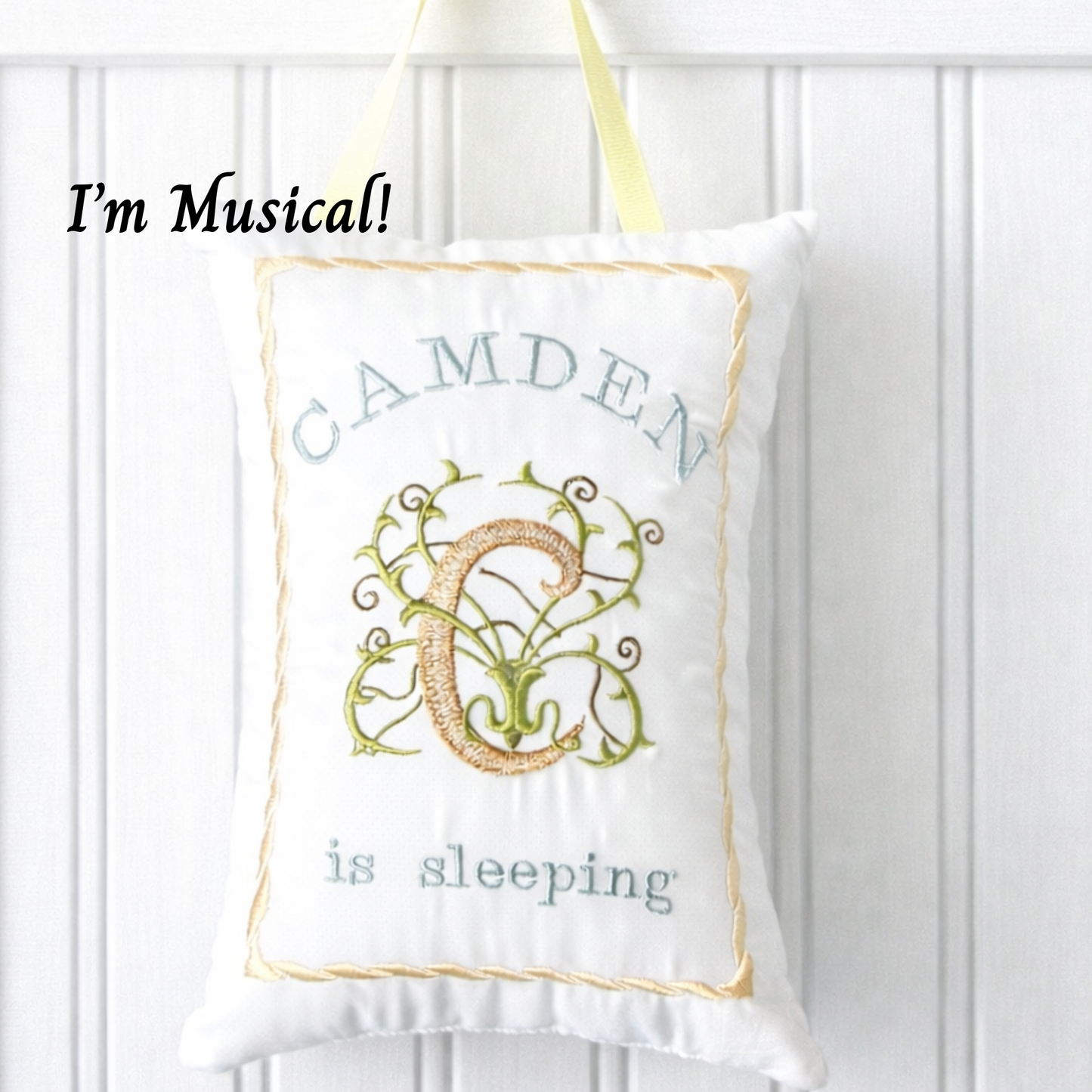 White music box pillow with embroidered name and decorative design on a white background