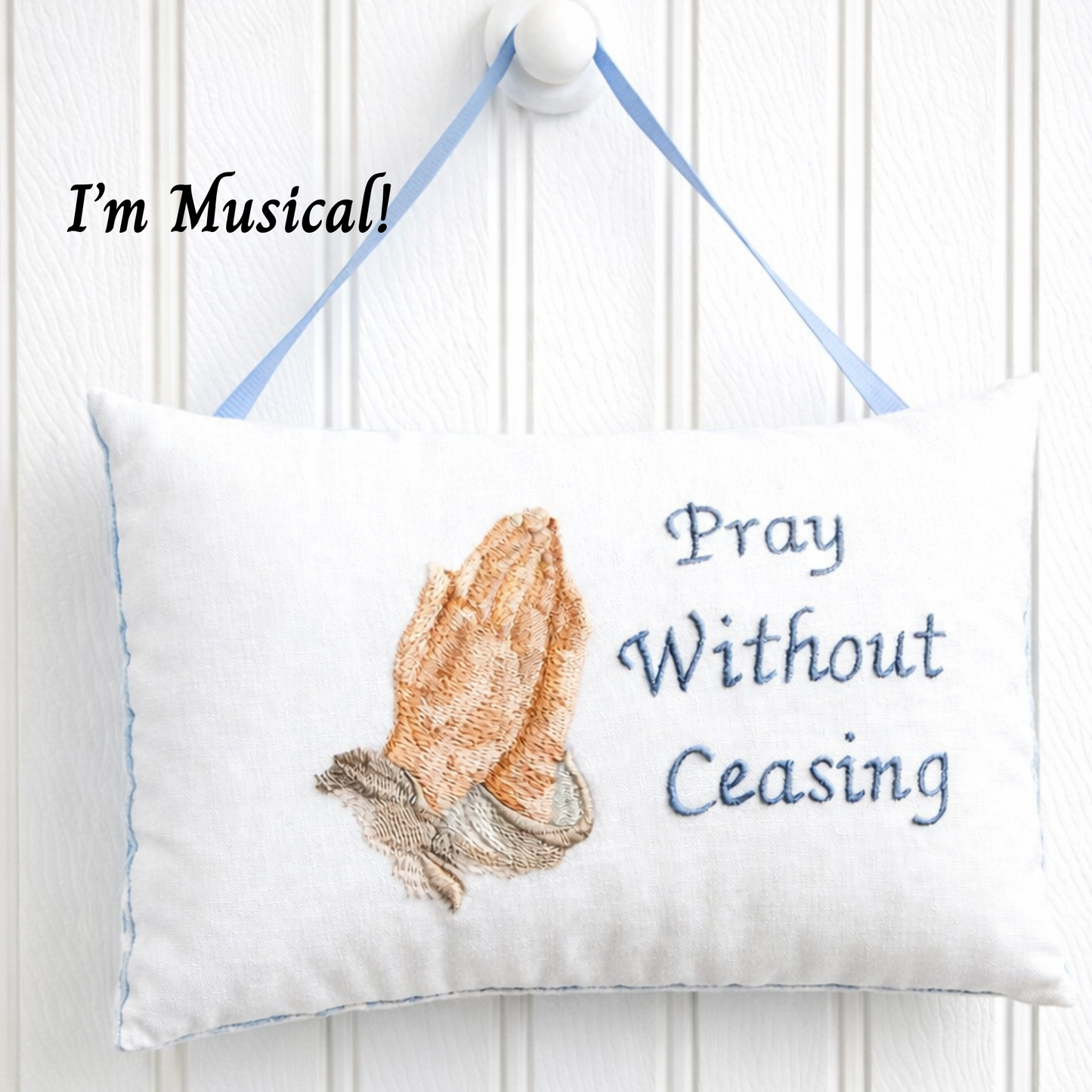 Decorative music box pillow with praying hands design and text on a white background