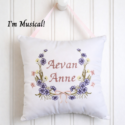 White music box pillow with floral design and embroidered name 'Aevan Anne' on a white background