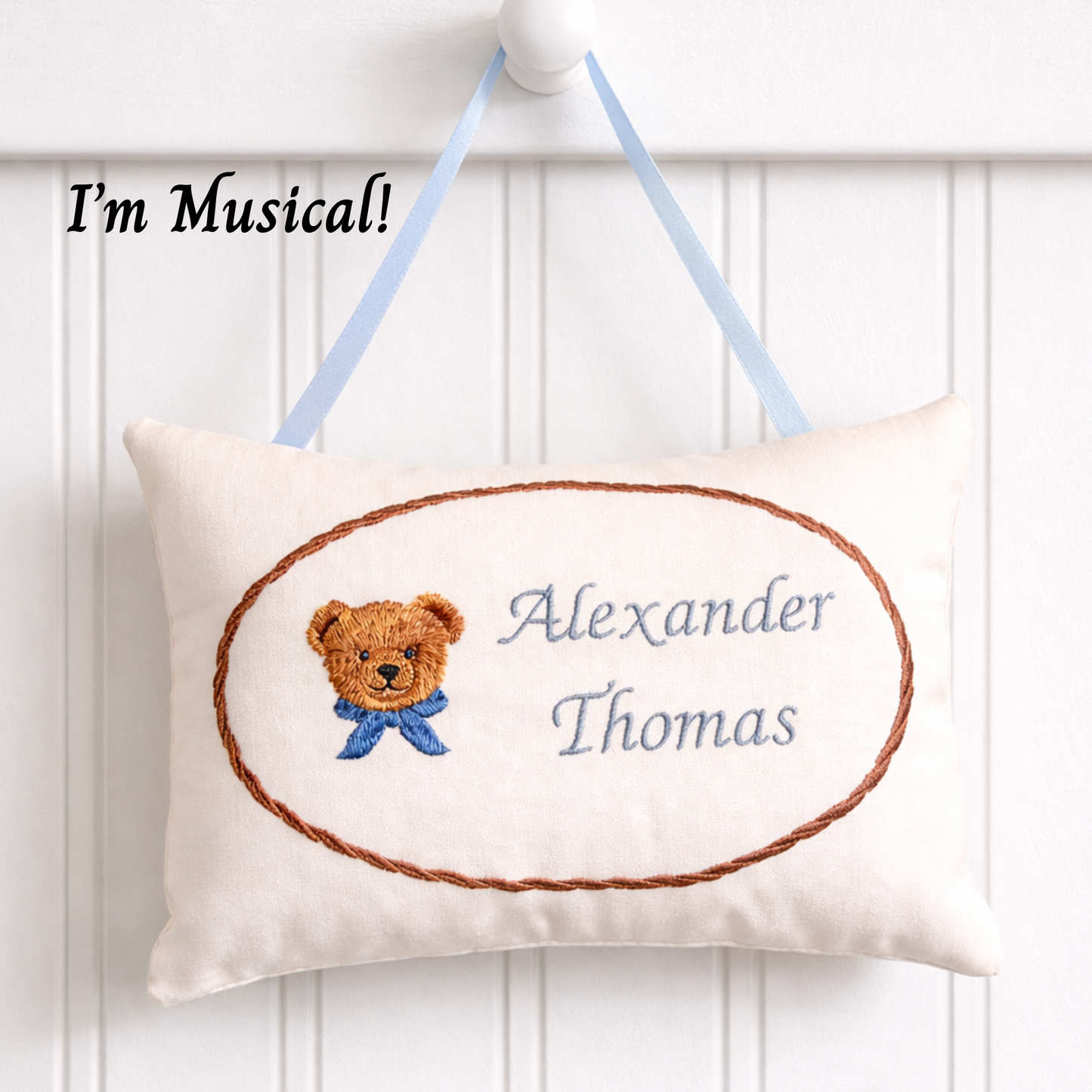 Decorative music box pillow with teddy bear illustration and embroidered name on a white background