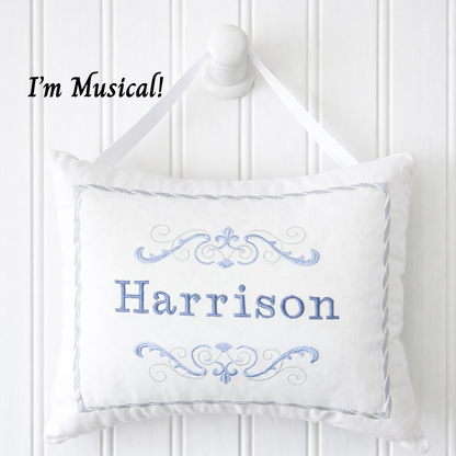 White music box pillow with blue embroidery and 'Harrison' text on a white wooden panel background