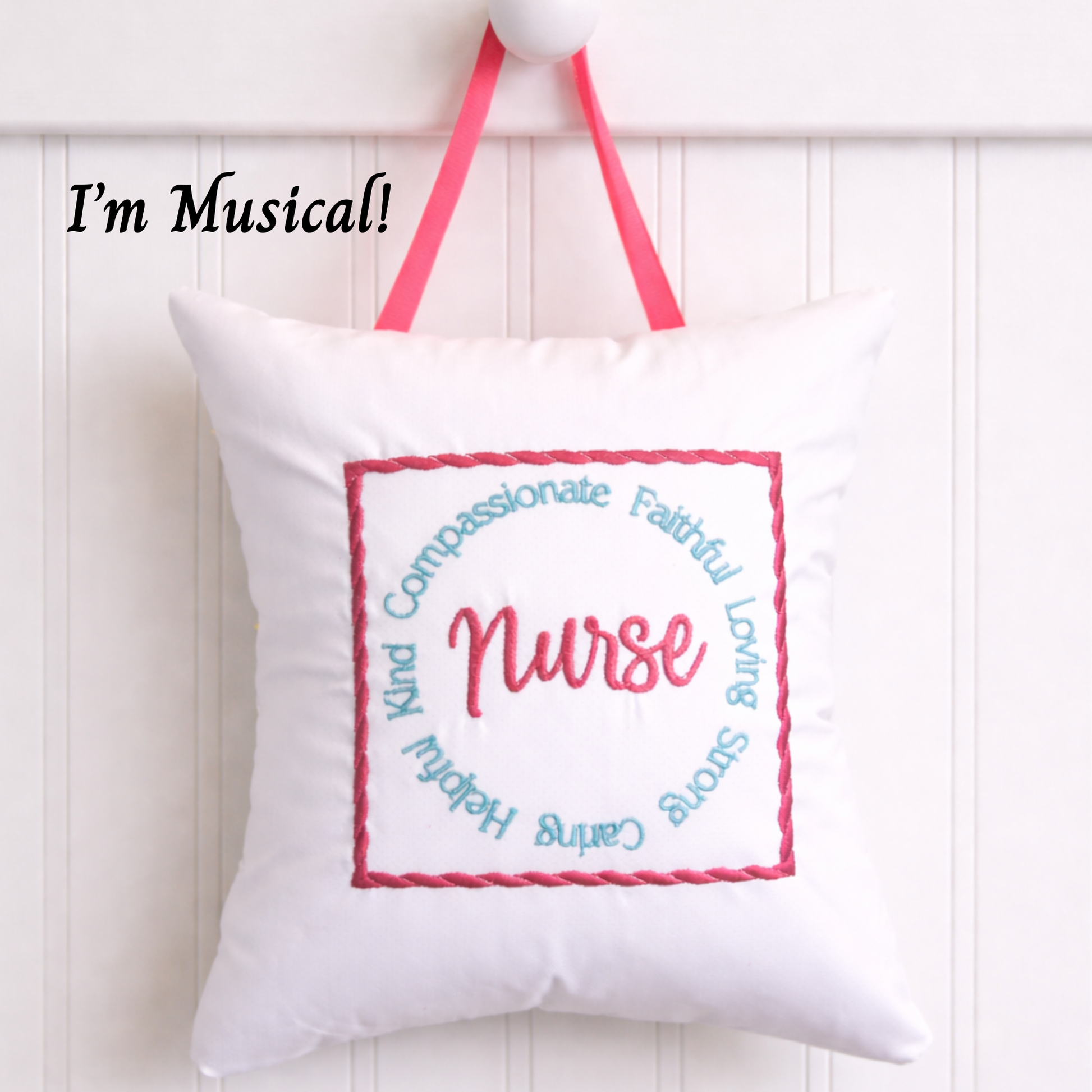 White music box pillow with embroidered text and pink straps on a white background