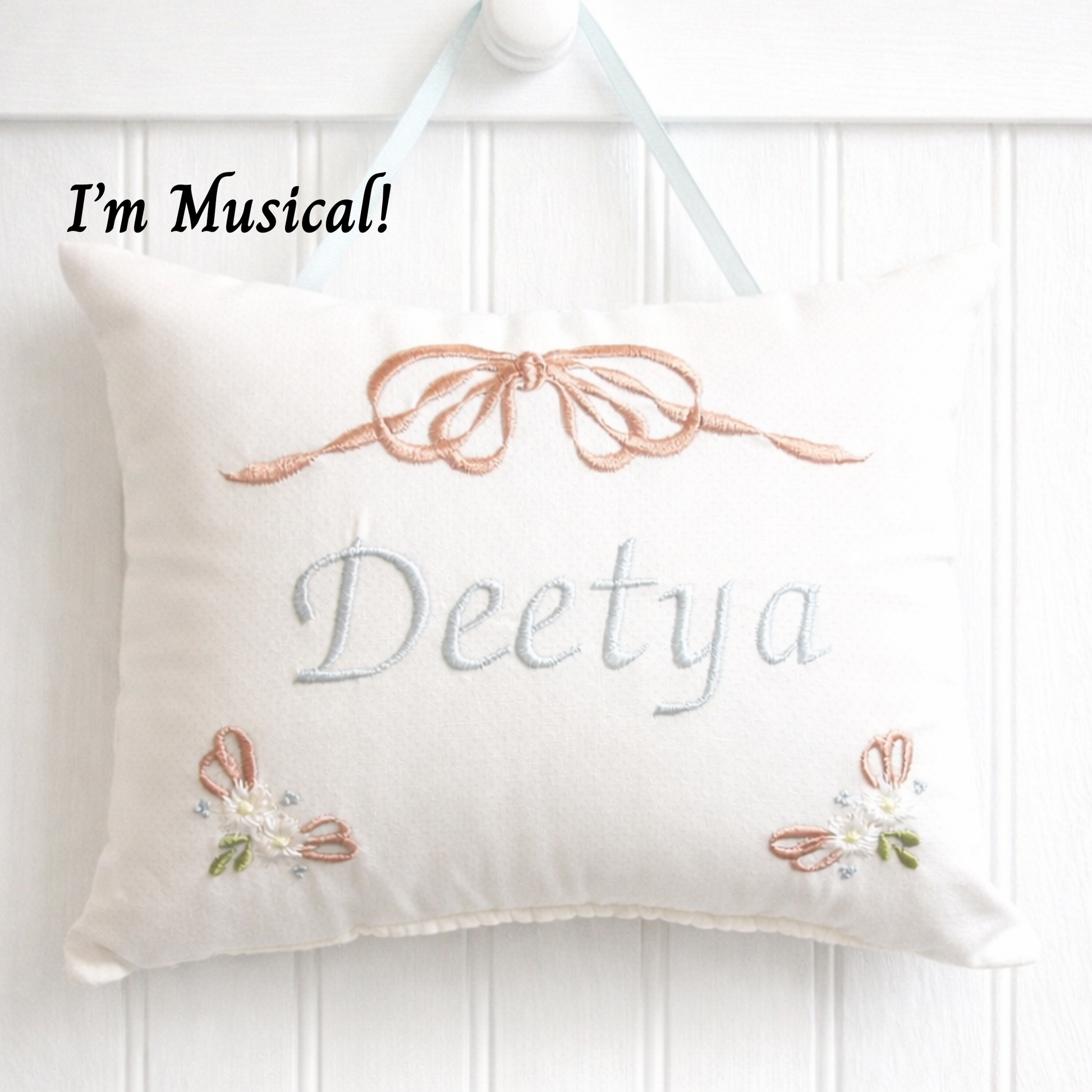Decorative music box pillow with embroidered name 'Deetya' and decorative elements on a white background.