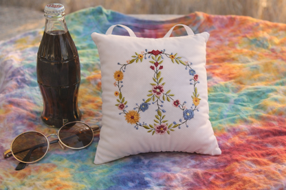 Decorative music box pillow with floral peace symbol design on a colorful fabric background with a bottle and sunglasses.